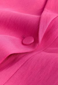 Gros plan d’un tissu rose vif avec un bouton recouvert de tissu et un détail de couture visible.