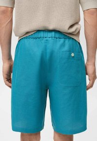 Pantaloni corti turchesi realizzati in tessuto leggero, dotati di una cintura elastica e di una singola tasca posteriore con chiusura a bottone.