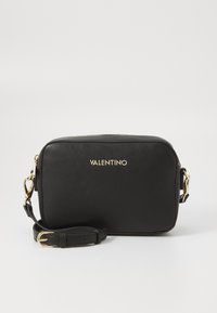 Sac bandoulière en cuir noir de forme rectangulaire, avec des métaux dorés et une bandoulière amovible. Présente un logo de marque sur le devant.