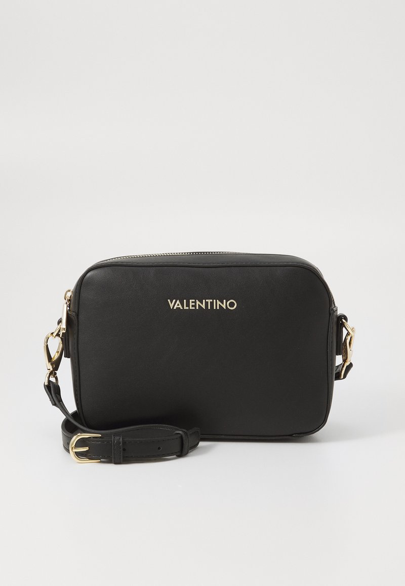 Sac bandoulière en cuir noir de forme rectangulaire, avec des métaux dorés et une bandoulière amovible. Présente un logo de marque sur le devant.