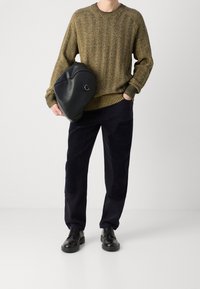 Sweter dziergany w oliwkowo-musztardowy wzór jodełki, zestawiony z granatowymi sztruksowymi spodniami z teksturowanymi dodatkami oraz czarnymi sznurowanymi butami.