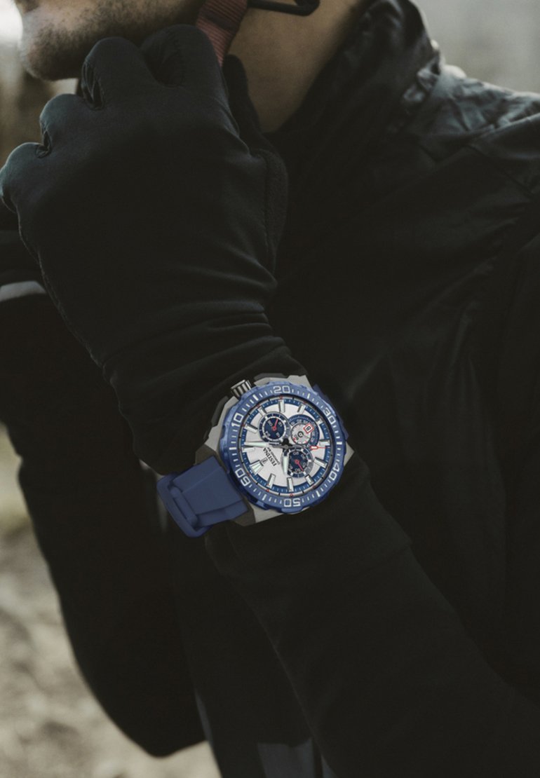 Reloj con correa de silicona azul, caja plateada, cara blanca y acentos azules; cuenta con tres subesferas y marcadores de horas en negrita.