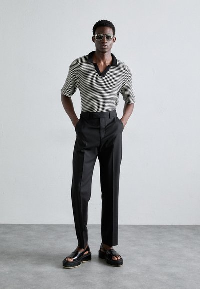 Polo de manga corta con patrón de pata de gallo en blanco y negro, combinado con pantalones negros de tiro alto y sandalias negras gruesas.