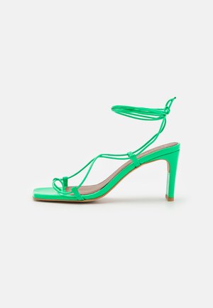 Πράσινη πατενταρισμένη δερμάτινη πέδιλη με τακούνι, με τετράγωνη μύτη, λεπτό λουράκι στο αστράγαλο και κομψό σχέδιο. Διαθέτει ψηλό στιλέτο τακούνι και ελάχιστες λεπτομέρειες.