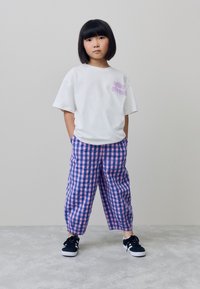 Witte oversized T-shirt met de tekst "Vibe Check" in paars, gecombineerd met loszittende roze en blauwe ruitjesbroek. Zwarte sneakers.