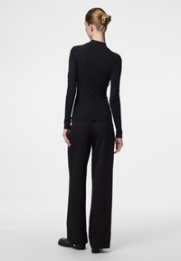Čierny top s dlhým rukávom a ryhovanou textúrou, spárovaný s voľnými čiernymi nohavicami. Model otočený chrbtom, predvádzajúci siluetu outfitu.