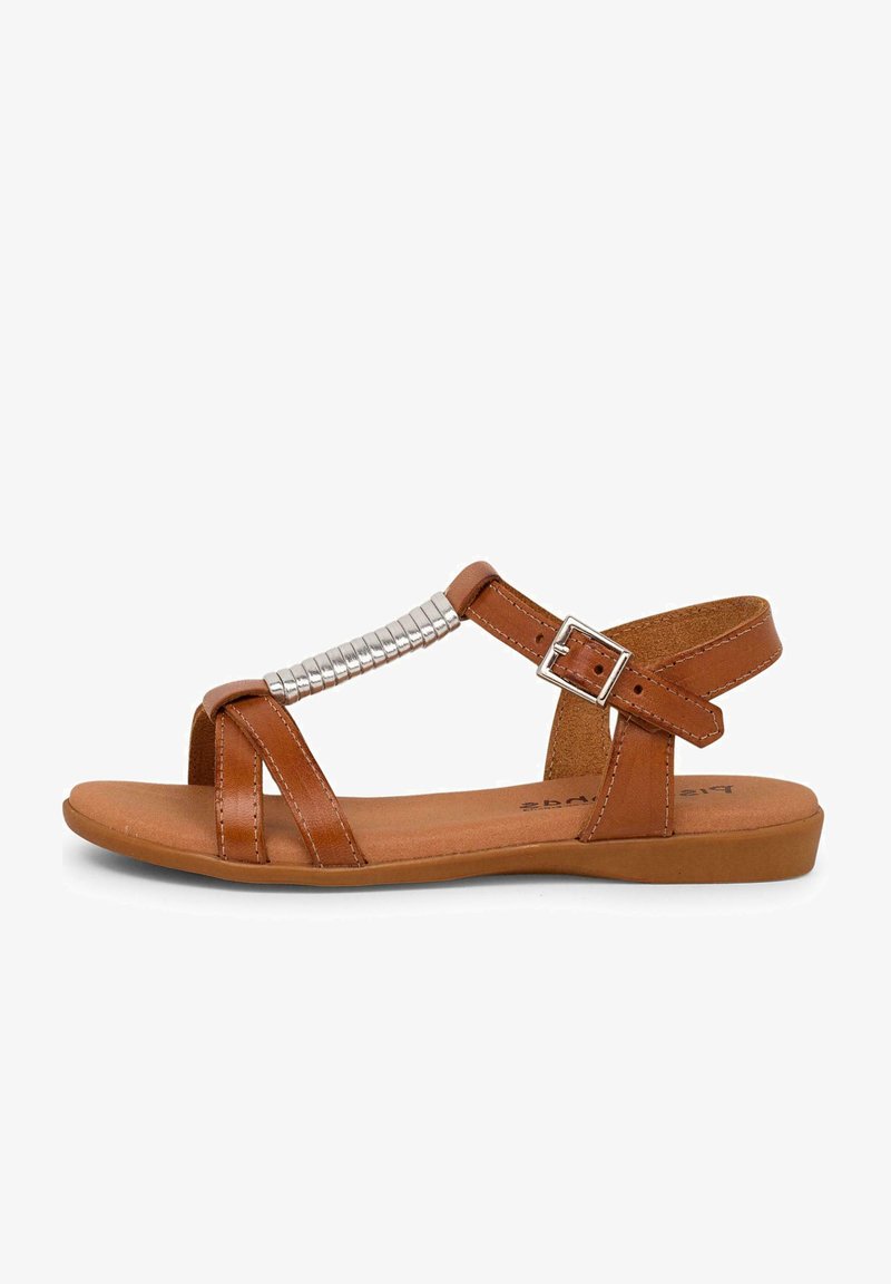 Brown leather sandals with a flat sole, featuring a decorative metallic accent and adjustable ankle strap. Detailed crisscross design.