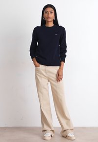 Pullover a maglia blu navy con scollatura rotonda, abbinato a pantaloni a gamba larga beige chiaro e sneakers platform bianche.