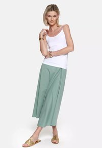Biały top na ramiączkach, jasna, zielona, lejąca się spódnica midi, złote sandały na płaskiej podeszwie. Gładka tekstura, minimalistyczny design i luźny krój.