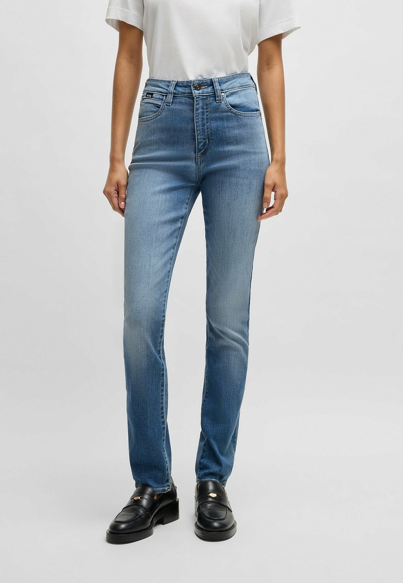 Jean bleu taille haute en denim clair, avec un design classique, jambe droite, style cinq poches, et une fermeture à glissière avec bouton.