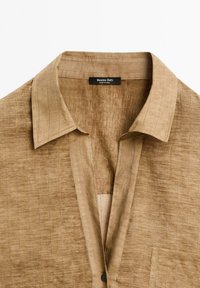 Brun texturerad skjorta med en strukturerad krage, med en knappslå och en liten bröstficka. Etiketten säger "Massimo Dutti, tillverkad i Kina."