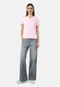 Rosa Poloshirt mit kurzen Ärmeln und V-Ausschnitt, kombiniert mit lockeren, hellgrauen Jeans. Verfügt über seitliche Taschen und einen lässigen Schnitt.