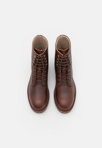 Hnědé kožené kotníkové boty na šněrování s hladkým povrchem, kulatou špičkou a pevným mosazným očkem na tkaničky, s ležérním designem.