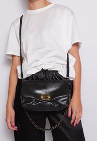 Borsa a tracolla in pelle nera dal design elegante, con una chiusura in ottone e una tracolla a catena, posizionata su uno sfondo bianco.