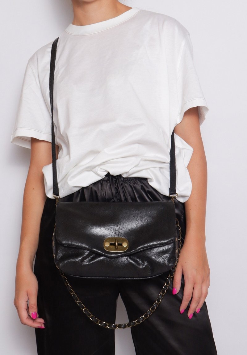 Borsa a tracolla in pelle nera dal design elegante, con una chiusura in ottone e una tracolla a catena, posizionata su uno sfondo bianco.