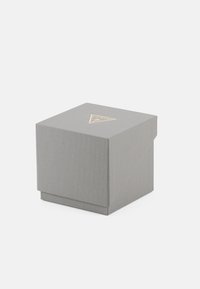Graue strukturierte Box mit einem dreieckigen goldenen Logo an der Oberseite. Sie verfügt über einen leicht schrägen Deckel und eine glatte, solide Basis.