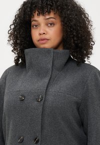Γκρι παλτό από μίγμα μαλλιού με ψηλό γιακά, διπλό κούμπωμα και μαύρα κουμπιά. Υφασμάτινη επιφάνεια με λεία υφή.
