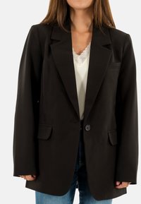 Blazer noir au design structuré, fermeture à bouton unique, revers crantés et deux poches avant. Tissu lisse et coupe décontractée.
