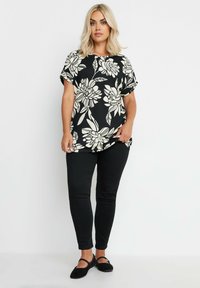 Top floreale nero con maniche corte, caratterizzato da un motivo di fiori crema; abbinato a pantaloni neri slim-fit e scarpe basse nere.