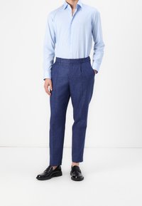 Ljusblå långärmad skjorta kombinerad med mörkblå texturerade byxor och svarta läderskor. Byxorna har pressveck fram och sidofickor.