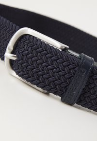 Cinto tecido azul-marinho com fivela de metal prateado e um detalhe em couro escuro com o nome da marca em relevo.