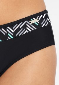 Zwarte bikini onderkant met een patroon tailleband met chevronontwerpen in zwart, grijs en mintgroen. Inclusief metalen logo-accent.