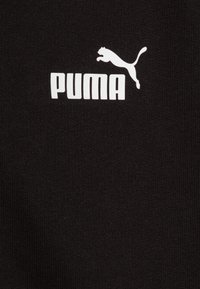 Tessuto nero con texture a coste presenta un logo "PUMA" bianco e un grafico di un gatto in salto, entrambi ben visibili sul materiale.