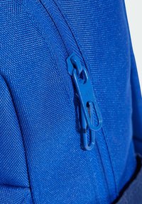 Modrý batoh z textílie s textúrovaným povrchom, obsahujúci modrý ťahák zipsu a detaily šitia. Detailný záber na oblasť zipsu.