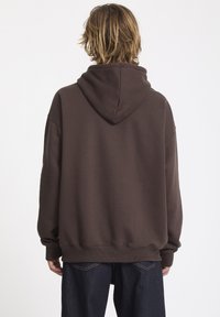 Sweat à capuche marron avec une coupe ample, doté d'une poche kangourou, de poignets côtelés et d'un design sans coutures à l'arrière.