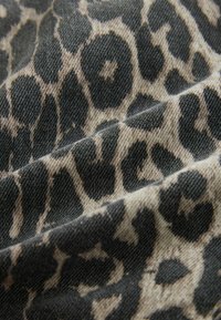 Tissu à motif léopard dans des nuances de beige et de noir, présentant une surface texturée avec des motifs de tissage visibles et des plis.