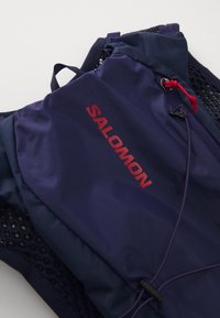 Navy blue Salomon running vest with mesh backing, featuring a red logo, adjustable straps, and slim, lightweight design.
