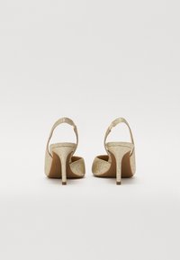 Sandales à talons hauts en paillettes dorées avec un dos ouvert, une bride de cheville réglable et un talon étroit et texturé. Intérieur lisse avec un design minimal.