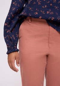 Blusa in blu navy con texture, motivo floreale e maniche arricciate, abbinata a pantaloni in velluto a coste rosa chiaro. Focus su tessuti e colori.