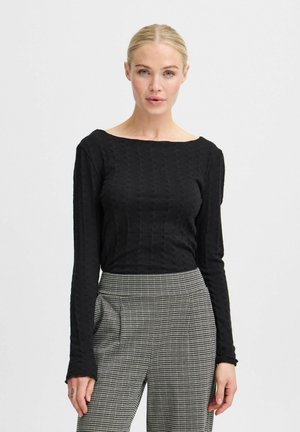 Haut noir à manches longues avec un décolleté bateau, présentant un motif texturé. Associé à un pantalon à carreaux taille haute.