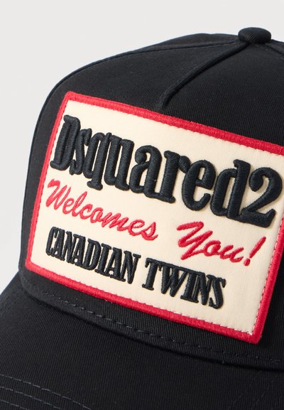 Casquette noire avec un patch blanc bordé de rouge affichant "Dsquared2 vous accueille ! JUMEAUX CANADIENS" en texte brodé noir et rouge.