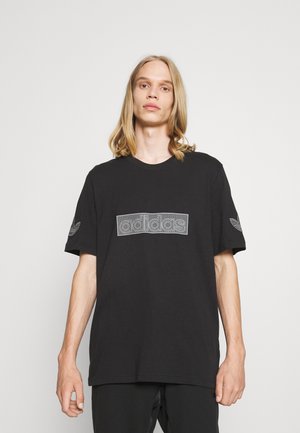 T-shirt in cotone nero con un grande logo adidas bianco testurizzato sul davanti e piccoli dettagli del logo sulle maniche. Maniche corte, vestibilità rilassata.