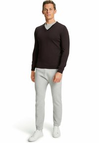 Pullover scuro marrone a scollo a V abbinato a pantaloni della tuta grigi chiari. L'outfit presenta una vestibilità rilassata e sneakers bianche per un comfort informale.