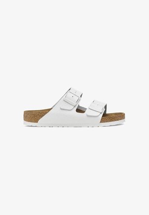 Sandales à glissière blanches à deux boucles avec un dessus en synthétique texturé, un pied de liège et une semelle extérieure en caoutchouc blanc. Design minimaliste avec des straps ajustables.