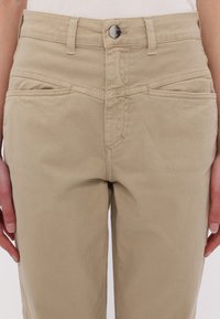 Beige bomuldsbukser med lynlås og knaplukning, for- og baglommer med syet detalje, glat tekstur.