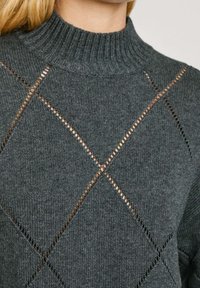 Grey knitted sweater with a high ribbed collar, features diamond patterns with cut-out details, and a soft textured finish.