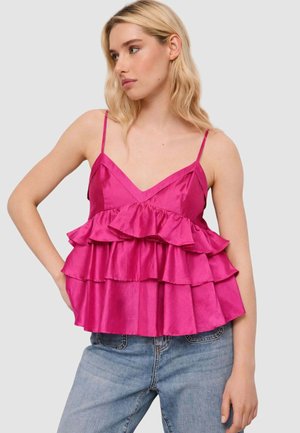 Donna che indossa una canottiera rosa acceso con volant a balze sottili abbinata a jeans azzurri, che guarda verso sinistra.