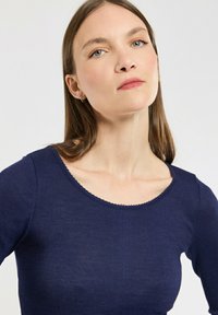 Haut à manches longues côtelé bleu marine avec un col rond orné de bordures en scallop. Texture douce avec une coupe ajustée.