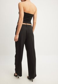 Čierny top bez ramienok skombinovaný s čiernymi elegantnými nohavicami s rovnými nohavicami a jemnými zadnými vreckami, umiestnený na neutrálnom pozadí.