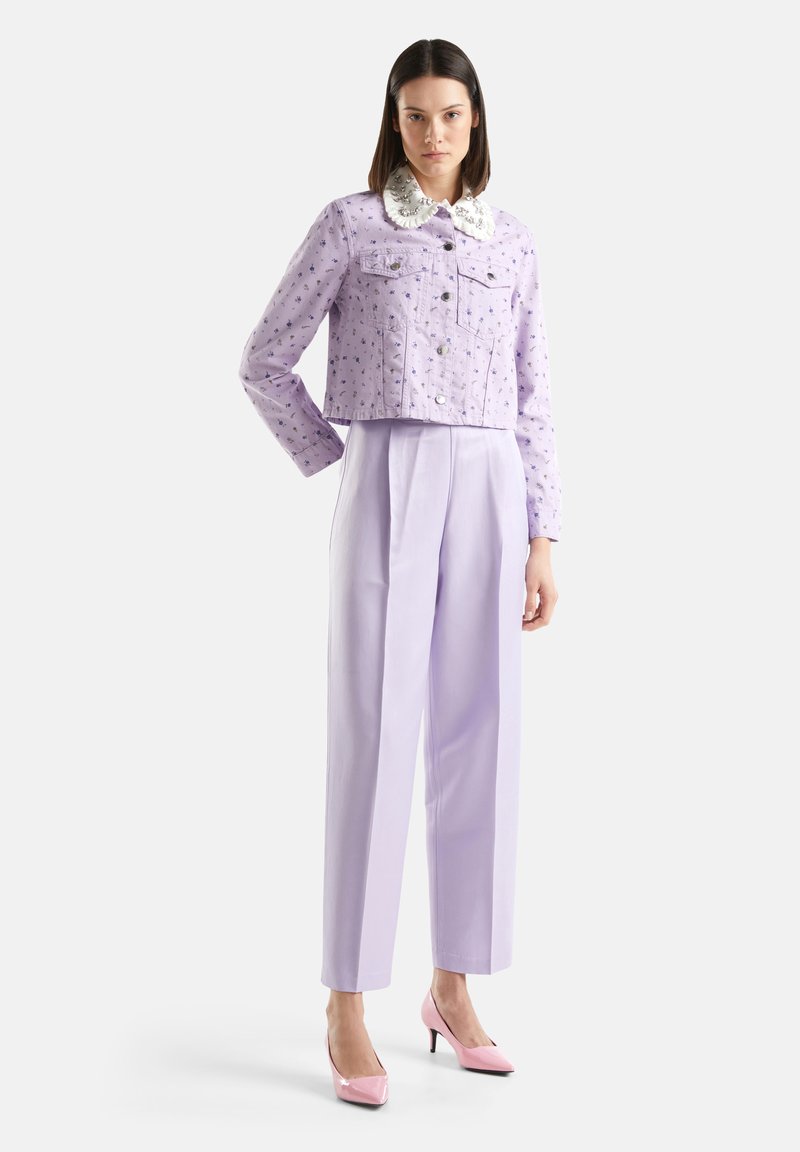 Giacca di denim lilla cropped con motivo floreale, colletto bianco e bottoni metallici, abbinata a pantaloni lilac a vita alta e tacchi rosa.