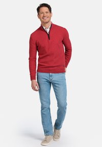Rode trui met een half-rits ontwerp, gedragen over een overhemd met boord, gecombineerd met lichtblauwe jeans en beige sneakers. Eenvoudige, gestructureerde stof.