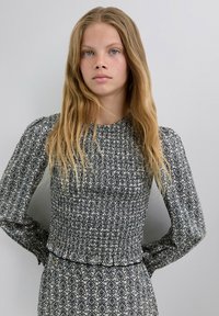 Blusa de manga larga con un patrón floral en blanco y negro, tela texturizada, cuerpo fruncido y un suave volán en el dobladillo.