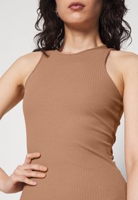 Abito a coste, senza maniche, di colore marrone chiaro. Forma aderente con scollatura alta. Texture liscia che esalta il contorno del corpo.