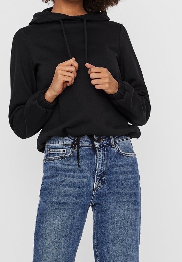 Sudadera negra con capucha, de manga larga y puños elásticos, combinada con jeans de mezclilla azul claro de corte clásico y diseño de cinco bolsillos.