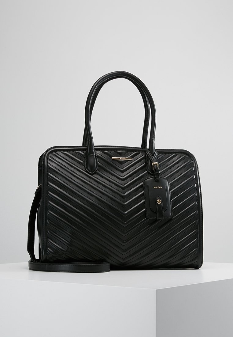 Sac à main en cuir noir avec coutures en chevrons, doubles poignées, une bandoulière détachable et une petite étiquette portant la mention Aldo, présenté sur une surface blanche.
