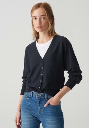 Marineblauwe cardigan met een V-hals, lange mouwen en een sluiting met vijf knopen, met ribgebreide manchetten en zoom, gecombineerd met lichtblauwe jeans.